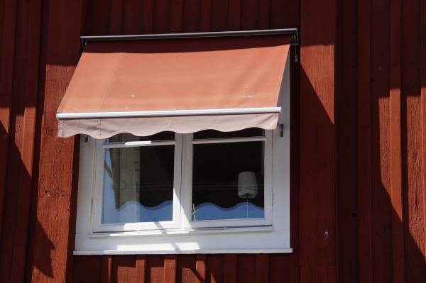 Röd fönstermarkis på ett rött trähus med vita knutar i Hyltebruk.